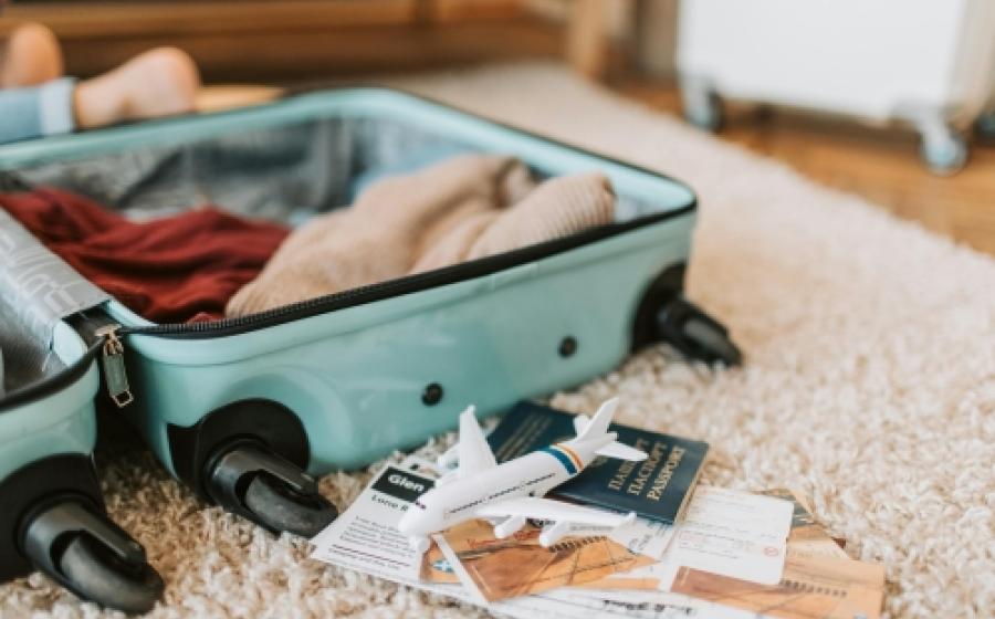 Green suitcase open on a carpet. It is filled with clothes and there are papers and passport next to it